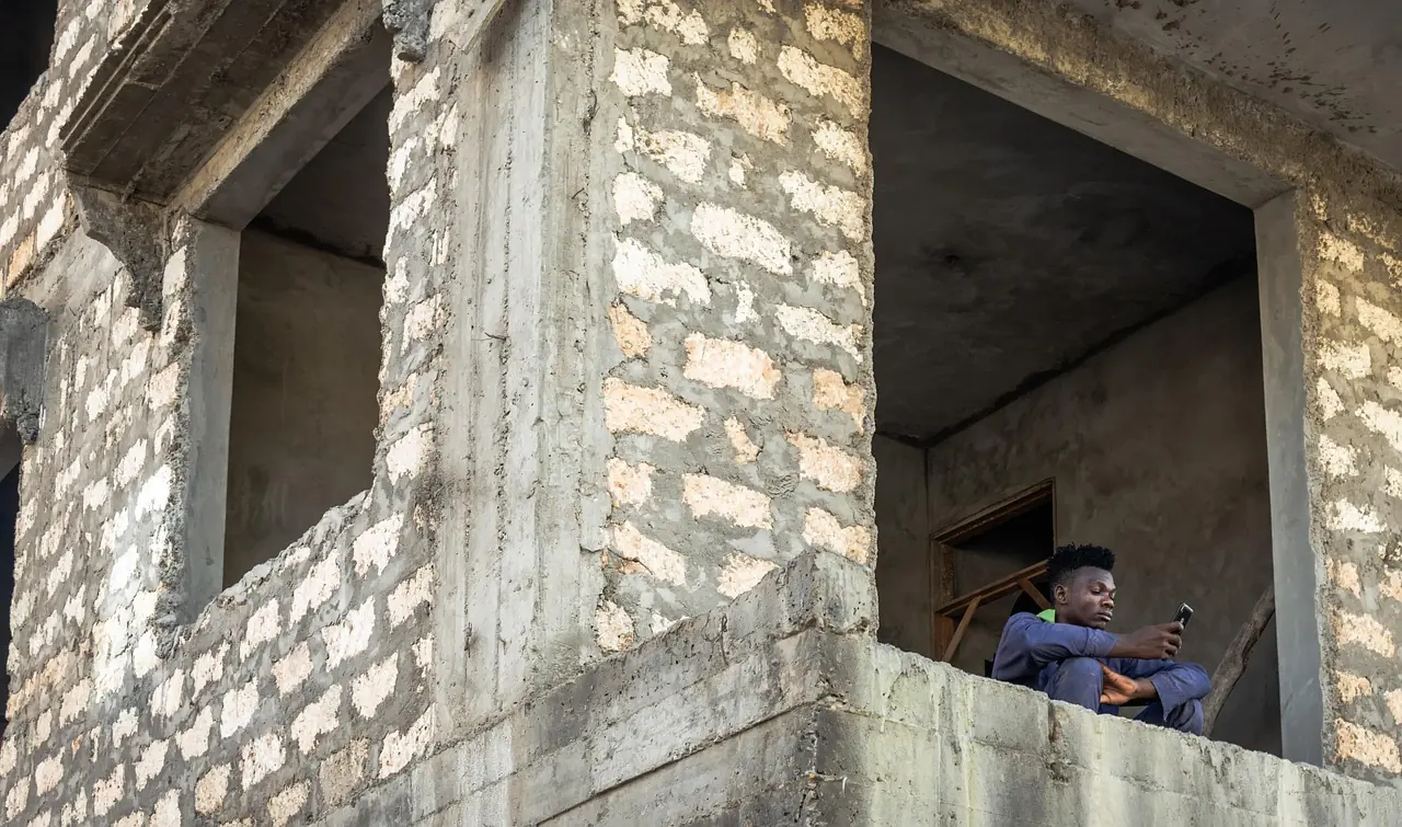A young man on his phone in a stone house under construction